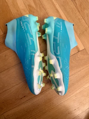 Turkosa Puma Ultra fotbollsskor - Säljer ett par grymma Puma Ultra fotbollsskor i turkos med vita och svarta detaljer. Skorna har strumpliknande skaft, plösfri design och mönstrad ovandel i syntetmaterial. Sulan är vit med gula dobbar för bästa grepp på planen. Perfekta för dig som vill sticka ut på matchen! Använda 3 mån