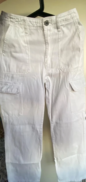 Vita cargobyxor med raka ben - Säljer ett par vita cargobyxor med raka ben och flera stora fickor på sidorna och bak. Byxorna har normal passform och är tillverkade i bomull, perfekta för en avslappnad och trendig look.