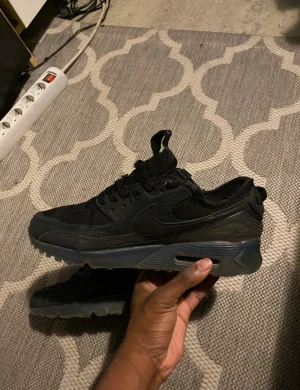 Svarta Nike Air Max sneakers - Säljer ett par svarta Nike Air Max sneakers med klassisk synlig luftdämpning i sulan. Skorna har mesh och syntet på ovandelen, snörning och en platt sula. Snyggt ton-i-ton med mörkgrå detaljer och rund tå. Perfekt för dig som gillar streetwear och sportig stil.