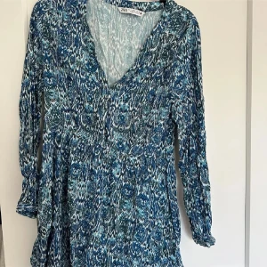 Blåmönstrad kortklänning från Zara - Supersnygg kortklänning från Zara med blått och vitt mönster. Klänningen har v-ringning, trekvartsärmar och ett flowy fall. Perfekt för dig som gillar boho-vibes och vill sticka ut med coolt print.