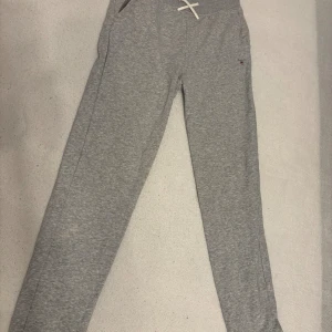 Grå mjukisbyxor från GANT med snörning - Snygga grå mjukisbyxor från GANT med broderad logga på benet och vit snörning i midjan. Byxorna har ribbad midja och är tillverkade i mjukt bomullsmaterial. Perfekta för chill eller träning, passar dig som gillar klassisk stil.