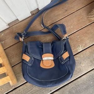 Mörkblå axelväska från Esprit i skinn - Snygg mörkblå axelväska från Esprit i mjukt skinn med kontrasterande ljusbruna detaljer och vita sömmar. Väskan har justerbar axelrem, lock med spänne och flera praktiska fack, inklusive innerficka med dragkedja. Perfekt för dig som vill ha en stilren och rymlig väska. Som ny! Jättefint skick 💕💕Vinted #Bag #Fynd #Secondhand #fashion #VintedUK #selling #Kappa #Coat #Kappa #Jacka