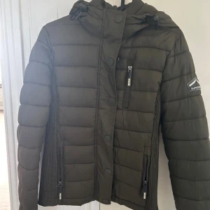 Superdry vinterjacka  - Mörkgrön jacka från Super dry i storlek Xs, (ljuset gör att den ser mer åt det gråa hållet) Bra skick och har en midja som går åt