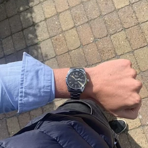 Svart och silver klocka från Doventi  - Stilren klocka från Doventi med svart urtavla och datumvisning. Klockan har en rund form och ett klassiskt armband i silverfärgad metall. Quartz-urverk och tydliga indexmarkeringar gör den både snygg och praktisk.