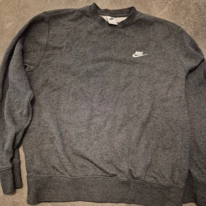 Grå Nike sweatshirt med logga - Mysig grå sweatshirt från Nike med klassisk vit logga på bröstet. Tröjan har rund halsringning, långa ärmar och ribbade muddar vid ärmslut och nederkant. 