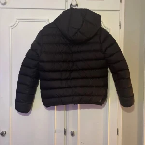 Svart Colmar pufferjacka med huva - Svart pufferjacka från Colmar Originals. Skulle säga att storleken är S och passar mig perfekt som är 163 cm lång. Jackan har en snygg, quiltad design med huva och dragkedja framtill. Två praktiska fickor med dragkedja och Colmar-logga på ärmen. Perfekt för kalla dagar och riktigt chill stil.