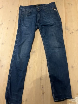 Replay Anbass jeans blå, storlek 31 - Snygga Replay Anbass jeans i mörkblå tvätt med klassisk femficksdesign och raka ben. Jeansen har en läderpatch bak med Replay-logga och detaljerade sömmar på bakfickorna. Materialet är slitstarkt denim och passformen är normal. Skick 9/10