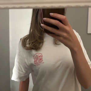 Vit t-shirt från Sweet SKTBS - Vit t-shirt från Sweet SKTBS med röd tryckt text på bröstet och ryggen. Klassisk passform med rund hals och korta ärmar. Tillverkad i mjuk bomull, perfekt för en avslappnad streetstil.