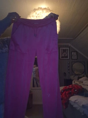 Rosa mjukisbyxor med snörning - Rosa mjukisbyxor med snörning i midjan och stora fickor både fram och bak. Byxorna är i ett mjukt material och har en relaxed passform, perfekta för chill dagar. Snygg och enkel design som är lätt att matcha med en hoodie eller t-shirt. Har ett litet hål i mellanbenen men det går jätte lätt att sy igen 