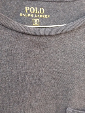 Mörkgrå t-shirt Polo Ralph Lauren S - Mörkgrå t-shirt från Polo Ralph Lauren i storlek S. Klassisk modell med rund hals, korta ärmar och bröstficka med rosa broderad logga. Tillverkad i mjuk bomull för en skön känsla. Perfekt basic med stilren look.