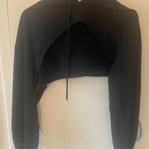 Svart croppad hoodie från SHEIN - Svart croppad hoodie från SHEIN med huva och snörning. Tröjan har lång ärm och är tillverkad i mjuk polyester och viskos. Perfekt för dig som gillar streetstyle och vill ha en edgy look. Snygg att matcha med höga jeans eller kjol.