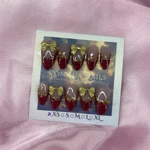 RubyBow (XS);Medium Almond - Snygga handgjorda press-on naglar i vinrött och nude med glansig finish. Dekorerade med glittriga guldrosetter och små gulddetaljer. Mandelformade och finns i XS: 14 mm, 11 mm, 11,5 mm, 10 mm, 8 mm. Perfekt för dig som vill ha extra glam på naglarna.