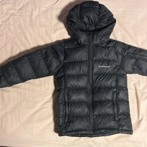 Svart Peak Performance dunjacka med huva - Säljer en svart dunjacka från Peak Performance med huva och dragkedja framtill. Jackan har ett quiltat mönster och logga på bröstet samt ärmarna. Perfekt för kalla dagar och har en clean, sportig look. Priset är inte hugget i sten och går självklart att förhandla 🤗