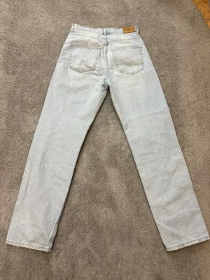 Ljusblå ripped jeans från Gina Tricot - Snygga ljusblå jeans från Gina Tricot med raka ben och slitna detaljer vid knäna. Klassisk femficksmodell med hög midja och Levi's patch bak. Perfekt för dig som gillar en avslappnad och trendig look.