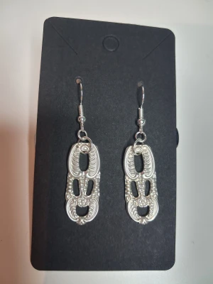 Handgjorda örhängen återbruk vintage - Egentillverkade örhängen gjorda av skedar i nysilver. Örhänget består av en liten blomma samt snirklar. Hänget är ca 3cm. Öronkroken är nickelsäker och aldrig använda. Blir en unik accessoar.