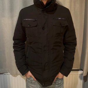 J.Lindberg Fieldjacka - En klassisk fieldjacka i fin mörkbrun färg i strl M. Det är två nedre knappar som saknas som lätt och billigt går att åtgärda hos en skräddare. Dock så kan man stänga jackan som vanligt. Alltså inga konstigheter så. Jackan är i 7/10 con därför har den ett schysst pris!