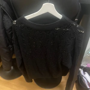 Svart stickad tröja från KappAhl XS - Svart stickad tröja från KappAhl i storlek XS. Tröjan har ett snyggt hålmönster över hela plagget och ribbad kant vid halsen. Perfekt för dig som gillar en klassisk look med lite extra detaljer. Långärmad och mjuk i materialet.