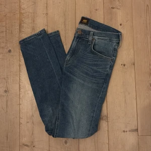 Blå Lee jeans - Snygga blå jeans från Lee med klassisk femficksdesign och brunt läderpatch bak. Slim fit