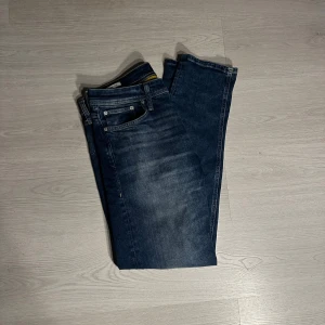Tapered Mike blåa - Snygga blå jeans från Jack & Jones med tapered Mike passform och klassisk femficksdesign. Jeansen har en mörk tvätt med lätt slitning och kontrastsömmar. Perfekt för dig som gillar en modern och avslappnad stil. Materialet är robust denim som sitter skönt hela dagen.