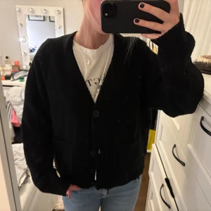 Svart kofta från Uniqlo, storlek S - Mysig svart kofta från Uniqlo i storlek S. Koftan är stickad med två stora fickor framtill och stängs med knappar. Perfekt för lager-på-lager och har en klassisk, avslappnad passform med långa ärmar.