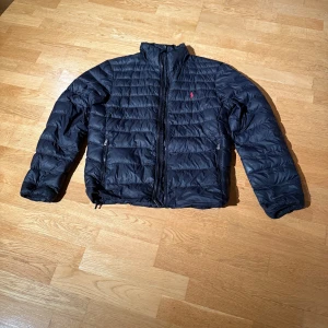 Svart dunjacka från Polo Ralph Lauren - Stilren svart dunjacka strl S från Polo Ralph Lauren med röd broderad logga på bröstet. Perfekt för kyliga dagar. 