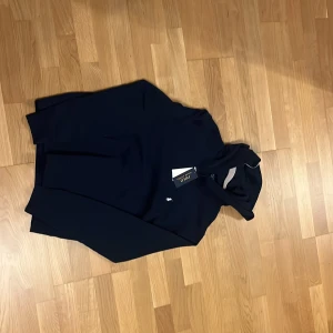 Marinblå hoodie från Polo Ralph Lauren. Barn storlek  - Snygg marinblå hoodie från Polo Ralph Lauren i storlek XL. Klassisk design med huva, lång ärm och en liten vit logga broderad på bröstet. Mjuk och skön bomullskvalitet, perfekt för chill dagar. Taggen sitter kvar och tröjan har en rymlig passform.