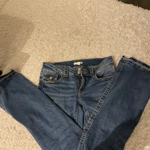 Blå bootcut jeans från Gina Tricot - Snygga blå jeans från Gina Tricot i bootcut-modell med klassisk femficksdesign och kontrastsömmar. Jeansen har normal passform och är tillverkade i slitstarkt denimtyg med lätt tvättad look. Perfekta för dig som gillar en tidlös stil.