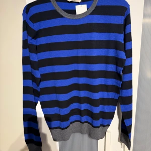 Randig blå och svart tröja H&M - Snygg långärmad tröja från H&M med breda blå och svarta ränder. Rund halsringning och grå ribbad kant vid hals och nederdel. Perfekt för dig som gillar en chill och stilren look. Materialet är mjukt och känns skönt mot huden.