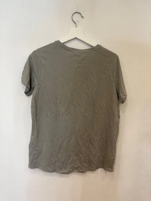 Grå t-shirt från Amisu med tryck - Snygg grå t-shirt från Amisu med rund hals och korta ärmar. Framsidan har ett stilrent tryck med texten 'HOME IS WHERE THE ♥ IS' i vitt. Mjuk och skön bomullskvalitet, perfekt för en chill look. Enkel design som funkar till jeans eller shorts.