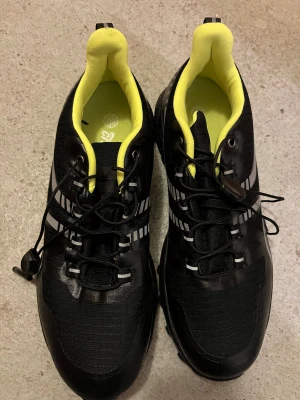 Svarta Crivit sneakers med grov sula - Säljer ett par svarta sneakers från Crivit med coola vita detaljer och neongul insida. Skorna har grov mönstrad sula för extra grepp och snörning med snabblås. Materialet är syntet och textil, perfekt för dig som gillar att vara aktiv utomhus.