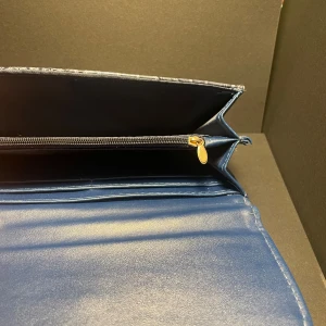 Blå plånbok med krokopräglat mönster - Snygg blå plånbok med krokopräglat mönster och tryckknapp. Flera fack för kort och sedlar samt ett myntfack med dragkedja. Perfekt för dig som vill ha en stilren och trendig accessoar i väskan.