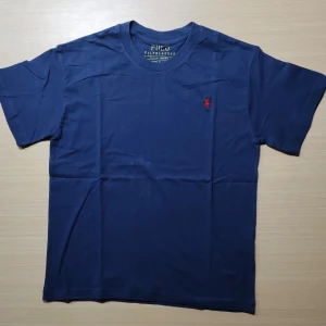 Svart t-shirt Polo Ralph Lauren S - Svart t-shirt från Polo Ralph Lauren i slim fit-modell. Klassisk design med rund hals och röd broderad logga på bröstet. Tillverkad i mjuk bomull som känns skön mot huden. Perfekt för dig som gillar stilrena och tidlösa plagg.