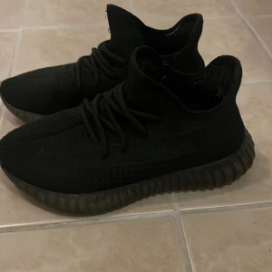 Svarta Adidas Yeezy Boost 350 sneakers - Säljer ett par svarta Adidas Yeezy Boost 350 sneakers med stickad ovandel och chunky, räfflad sula. Skorna har snörning och en modern, sportig siluett som är riktigt populär. Perfekt för dig som gillar streetwear och vill ha en clean look.