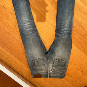 Blå tiger of Sweden jeans med slitningar - Säljer ett par blå skinny jeans från tiger of Sweden med slitningar på knäet och råa benslut. Jeansen har en ljus tvätt med snygga detaljer på bakfickorna. Perfekt för dig som gillar en avslappnad och trendig look.