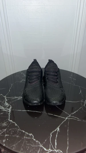 Nike Air Max 270 svarta sneakers - Svarta Nike Air Max 270 sneakers med mesh-ovandel och synlig Air-enhet i hälen. Snygg sportig design med snörning och platt sula. Perfekt för dig som gillar en enkel daglig stil, eller att ha på sig dem överlag och vill ha bekväma skor med modern look. 