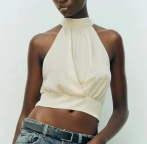 Slutsåld Zara satin halterneck topp - Säljer en  croppad halterneck topp med omlott-design och hög hals. Perfekt för en kväll ute eller fest men ochså bara för att sätta en lite touch på din outfit. Toppen är i storlek xs och har aldrig kommit till användning då jag vuxit ur den sen jag köpte den. Artikeln har även utgått ur Zaras sortiment. Köptes ungerfär vintern 2023/februari 2024 