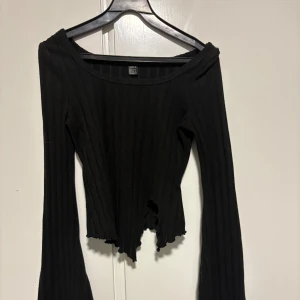 Svart ribbad långärmad topp - Svart ribbad långärmad topp från Shein med offshoulder-skärning och vågig, asymmetrisk nederkant. Toppens material är mjukt och stretchigt, perfekt för en trendig och avslappnad look. (Använt 1 gång) priset kan diskuteras.
