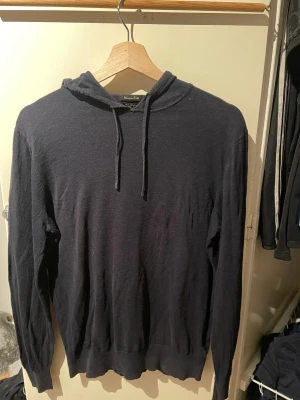 Mörkblå hoodie från Massimo Dutti - Snygg mörkblå hoodie från Massimo Dutti med huva och snörning. Tillverkad kashmir som känns mjuk mot huden. Tröjan har långärmad passform och ribbade muddar vid ärmslut och nederkant. Perfekt för chill dagar.