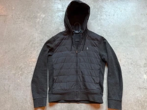 Svart Ralph Lauren cardigan  - Svart cardigan från Polo Ralph Lauren med quiltad front och broderad logga på bröstet. Jackan har dragkedja, snörning i huvan och mjuka ärmar. Inga synliga defekter alls. 