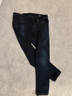 Dondup jeans - Säljer ett par svarta/mörkblå Dondup george jeans.Jeansens bakficka har en metallisk D-logga och midjan är normal. Perfekt för dig som gillar stilrena och moderna jeans. Obs jeansen är uppsydda ett par cm men det är lätt att sprätta upp!