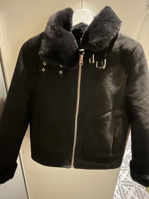 Svart teddyjacka från H&M med dragkedja - Svart teddyjacka från H&M med fluffig krage och muddar. Jackan har en snygg dragkedja framtill och fickor på sidorna. Utsidan påminner om mocka och insidan har ett varmt, lurvigt foder.