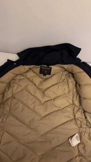 Mörkblå dunjacka från Woolrich - Säljer en mörkblå dunjacka från Woolrich den är i väldigt bra skick och är perfekt för vintern den är storlek M och passar L. Anledningen till att jag vill sälja den är att den inte passar mig längre. Priset kan diskuteras vid snabb affär!!