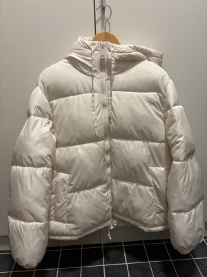 Vit dunjacka med huva - Vit pufferjacka med huva och dragkedja framtill.