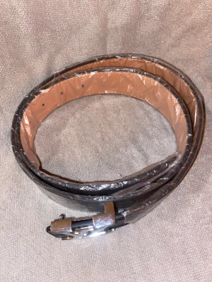 Louis Vuitton rutig svart skärp i skinn - Snyggt Louis Vuitton bälte i svart och grått med klassiskt rutigt mönster och LV-logga på spännet. Bältet är tillverkat i skinn med en stilren form och detaljerad finish. Perfekt accessoar för dig som vill ha en lyxig och trendig look.