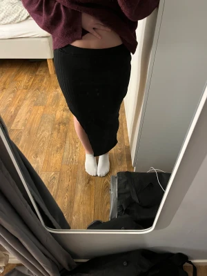 Svart ribbad långkjol - Säljer en svart långkjol med ribbad struktur och tight passform. Kjolen har en enkel, rak siluett och är gjord i ett mjukt, stretchigt material.