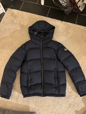 Mörkblå Colmar vinterjacka - Säljer en mörkblå pufferjacka från Colmar som är i toppskick! Den är använd ett par fåtal gånger och är i storlek XS. Det finns inga defekter på jackan och det är bara att höra av sig vid frågor och funderingar!