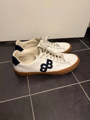 Vita sneakers från BOSS  - Snygga vita sneakers från BOSS med mörkblå B-logga på sidan och blå häl.  Inte särkilt använda, finns litet tecken på slitage på bild 5 annars är de utmärka! 