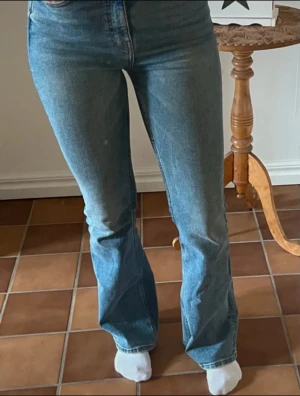 Blå bootcut jeans med hög midja - Snygga blå jeans med bootcut-modell och hög midja. Jeansen har klassisk femficksdesign och är tillverkade i ett mjukt denimtyg som sitter skönt. Perfekta för dig som gillar en tidlös och trendig look.