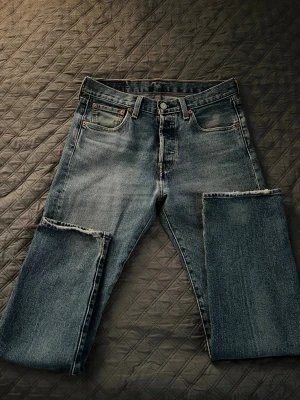 Levi's 501 blå jeans W29 L30 - Klassiska Levi's 501 jeans i mellanblå tvätt med raka ben och knappgylf. Jeansen har fem fickor, kontrastsömmar och den ikoniska röda Levi's-taggen på bakfickan. Materialet är slitstarkt bomullsdenim och passformen är straight.