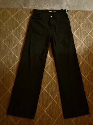 Svarta wide jeans från Infinity W28/L32 - Säljer ett par svarta jeans från Infinity i storlek W28/L32. Byxorna har en rak och bred passform med klassiska fem fickor, bälteshällor och knappgylf. Perfekta för dig som gillar en loose och avslappnad stil. Aldrig användt.